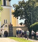 Menschen verschiedenen Alters ziehen in eine Wallfahrtskirche ein. Es ist Spätsommer.